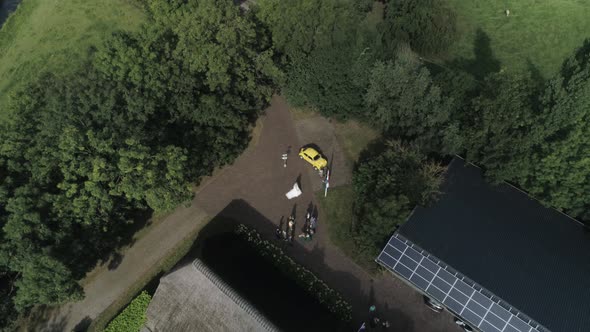 Aerial Zoom out of an Wedding with the Bride and Bridemaids Walking and a Yellow Car in background