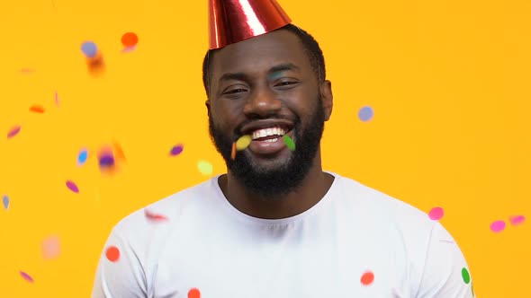 Happy Afro-American Man in Party Hat Under Falling Confetti, Birthday Surprise