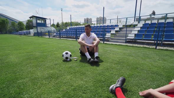 Young Boys Team Sitting on the Grass Players on a Training Football Field the Coach Instructs and