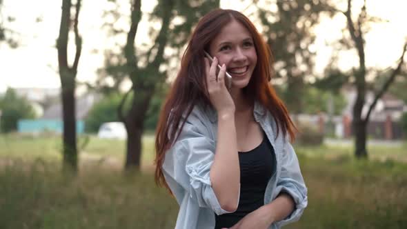 Relaxed Joyful Woman Laughing Talking on Phone Standing in Sunshine Outdoors