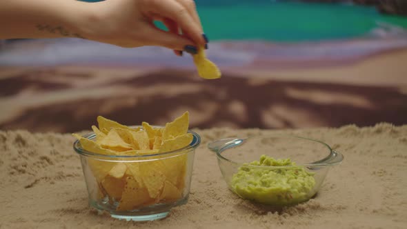 Female Hand Taking Nachos Dip with Guacamole Sauce on the Beach Near the Sea