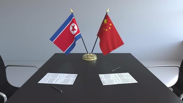 Flags of North Korea and China and Papers on the Table alt