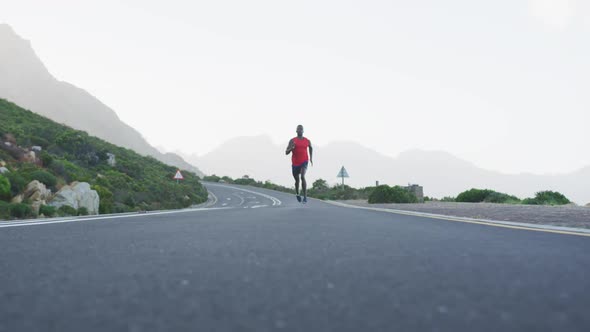 Fit african american man exercising running on a country road near mountains