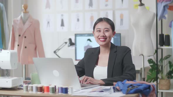 Female Designer In Business Suit Working On A Laptop And Smiling To The Camera While Designing Cloth