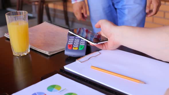 A male customer pays using NFC contactless payment technology on a smartphone.