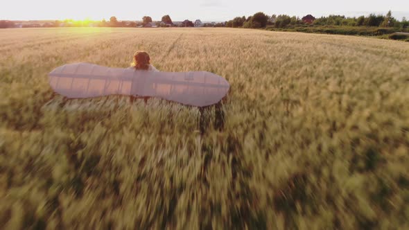 Aerial: Girl with Wings Running Through Wheat Field, Dreaming of Flying. Da Vinci Wings