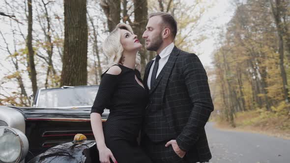 Portrait of Exquisite Lady Flirting and Posing at Happy Man at Car in Forest