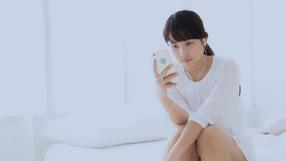 Young asian woman sitting happy earphone listening music with relax and enjoy in the bedroom.