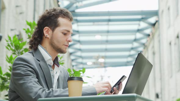 Young successful caucasian businessman works in an outdoor cafe using a computer