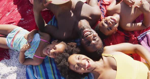 Portrait of smiling african american family lying on towels on sunny beach