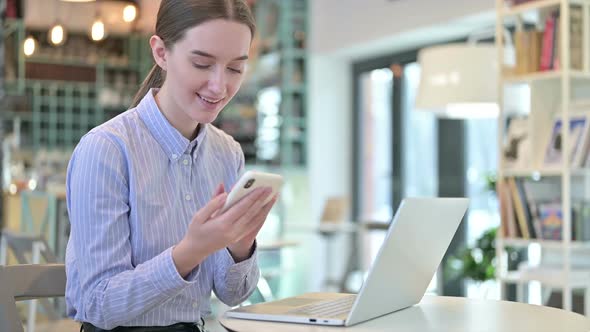 Young Businesswoman Using Smartphone with Laptop in Cafe