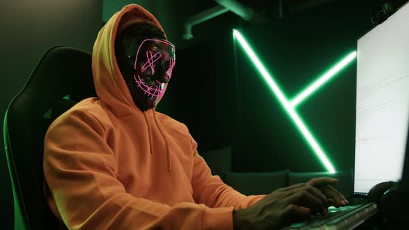 Hacker in an Orange Hood and with a Mask Hacking Databases Medium Shot Cyberterrorism Concept