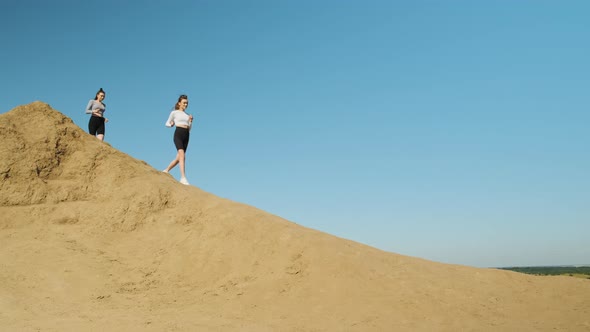 Two Slender Athletic Women in Sportswear and Black Shorts are Doing Marathon Run Running Down Sandy