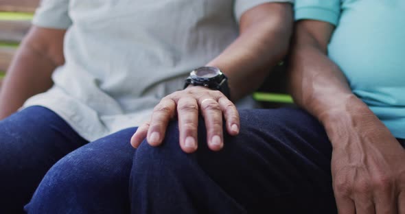 Video of midsection of biracial senior couple holding hands and sitting in garden