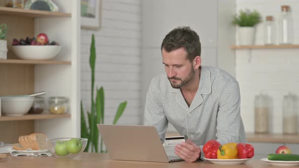 Man Making Online Payment on Laptop in Kitchen