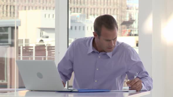 Businessman using laptop and making notes in office