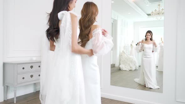 4K Asian woman lesbian couple trying on wedding dress in front of the mirror together at bridal shop