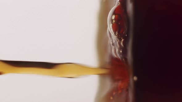 Experimental slow motion shot of a dark brown liquid getting poured into cup. Vertical video