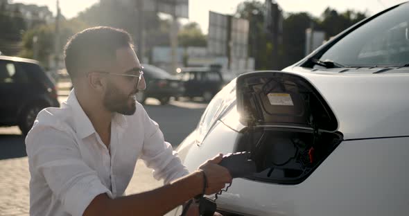 Young Arab Man Recharging White Electric Car at Parking Lot