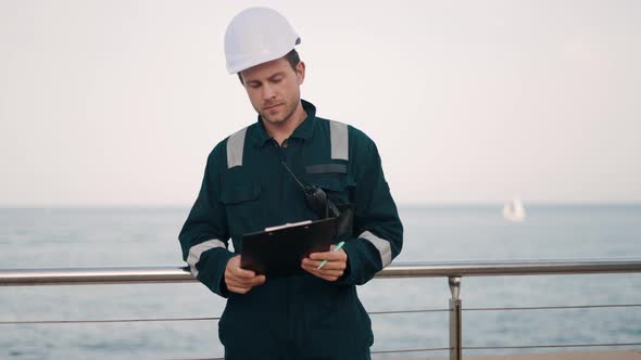 Port Inspector Standing at Sea Station with Clipboard and Vhf Radio Making Notes in Checklist