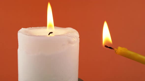 Two Burning Candles with a Bright Flame on an Isolated Orange Background