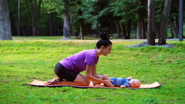 Mother doing baby gymnastics for her little son in green park