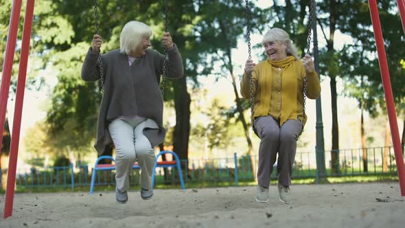 Two Elderly Women Laughing Riding Swings in Park, Elderly Friends, Retirement
