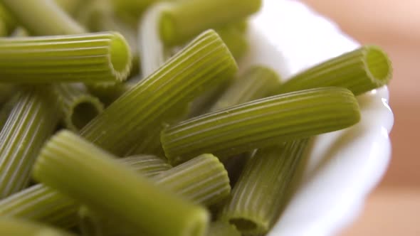 Uncooked dry green vegetable pea dough pasta falling in a heap in a white bowl on a wooden table