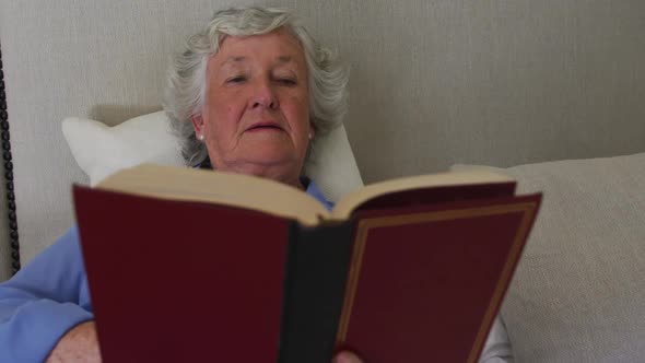 Happy caucasian senior woman at home enjoying reading book sitting up in bed in