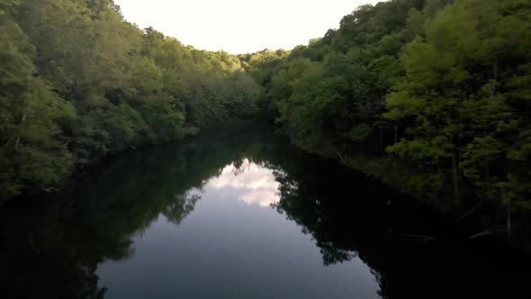 This is a aerial shot of a private lake with a little cabin on it surrounded by tons of forest.