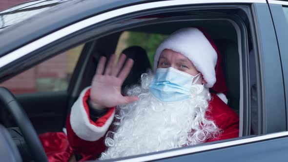 Joyful Santa Clause in Covid19 Face Mask Waving Looking at Camera Sitting in Car on Driver's Seat