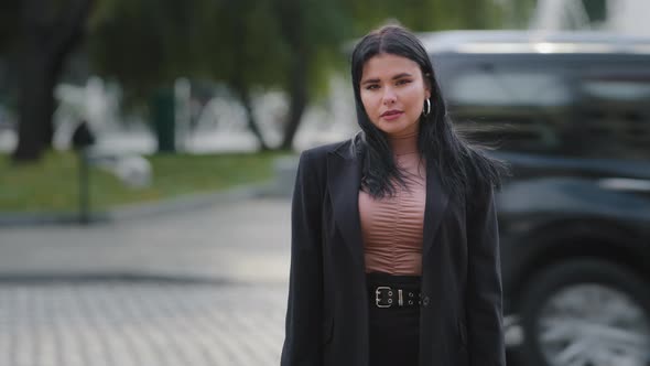 Young Confident Serious Hispanic Businesswoman in Business Suit Standing Outdoors Near Roadway
