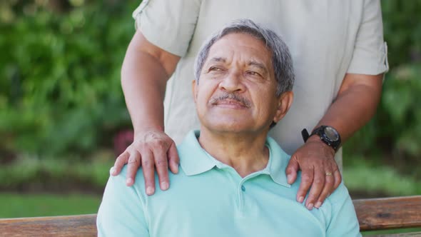 Video of happy biracial senior couple embracing and sitting on bench in garden