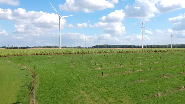 Drone rises over a  grass field filled with wind turbines on a fluffy cloud day.