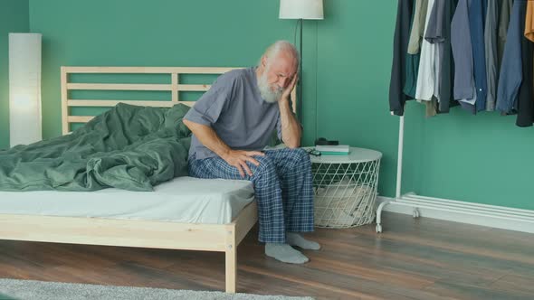 Tired Elderly Man Has Acute Headache While Sitting on Ahe Bed At Home