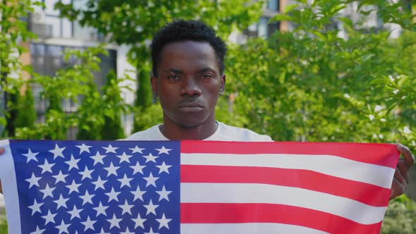 Close Up Afroamerican Man Holding an American Flag and Looks Camera in Summer