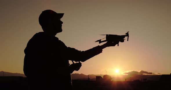 Silhouette of boy flying drone at sunset