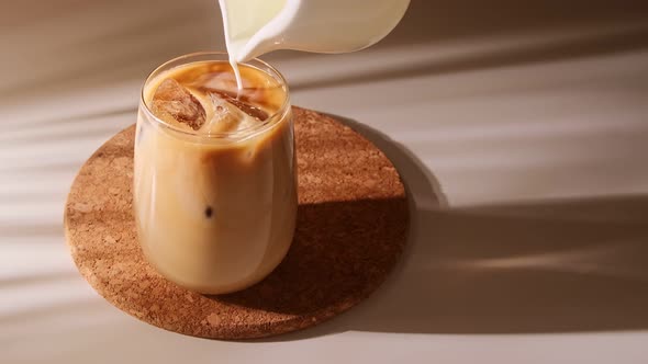 Milk cream is pouring into a iced coffee. Cold coffee drink