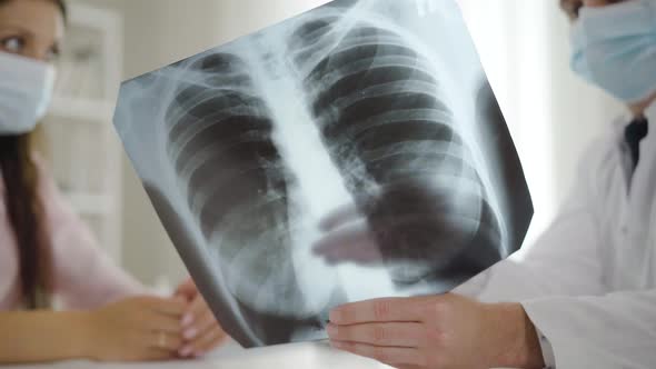 Close-up Lungs X-ray with Doctor and Patient in Face Masks Talking at the Background. Physician