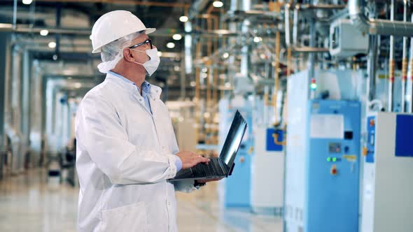 Male Engineer in a Hardhat is Using His Laptop in the Factory