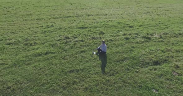 Low Orbital Flight Around Man on Green Grass with Notebook Pad at Yellow Rural Field