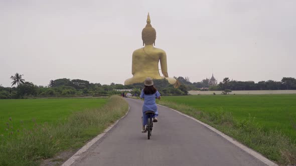 Asian woman cycling a bicycle near the Giant Golden Buddha in Wat Muang in Ang Thong