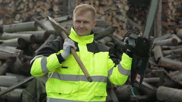 Lumberjack Worker. Man Woodcutter Holds Big Axe and Electric Chainsaw on His Hands. Firewood