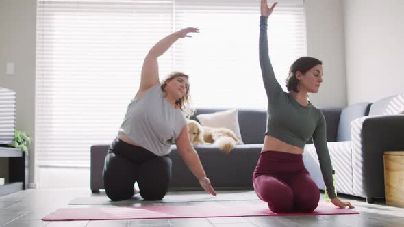 Caucasian lesbian couple keeping fit and stretching on yoga mat