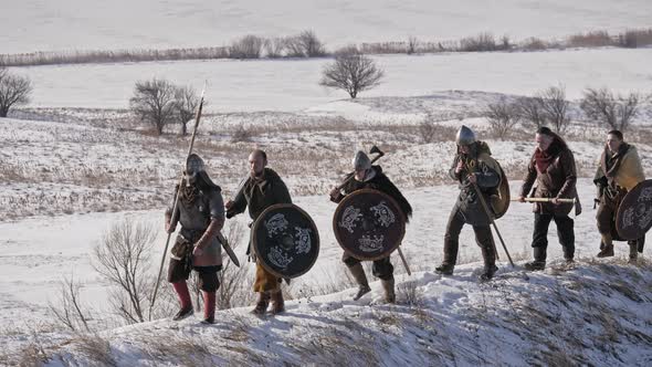 Group of Vikings with shields and swords going forward on the winter meadow. Male, leader.