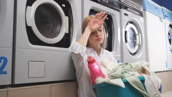 A Woman Sitting Next To a Washing Machine in a Public Laundry Room She Is Tired of Waiting