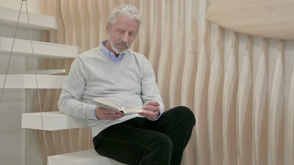 Old Man Reading Book While Sitting on Staircase