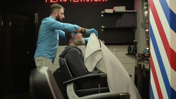 The master invites the client to sit in a chair for a hair and beard cut