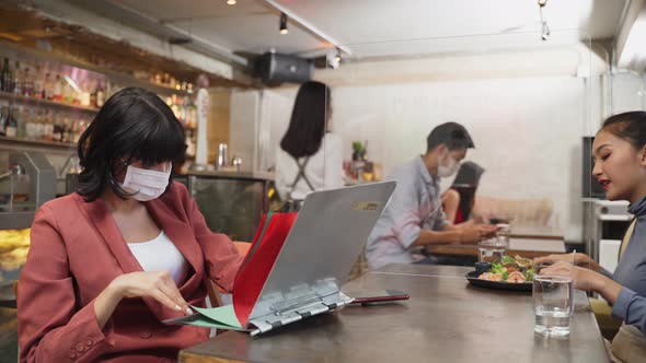 Waitress wear mask, serve food to customer sit on social distance table for new normal in restaurant