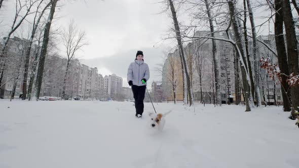 Happy Girl with Dog Running Along in Park Winter